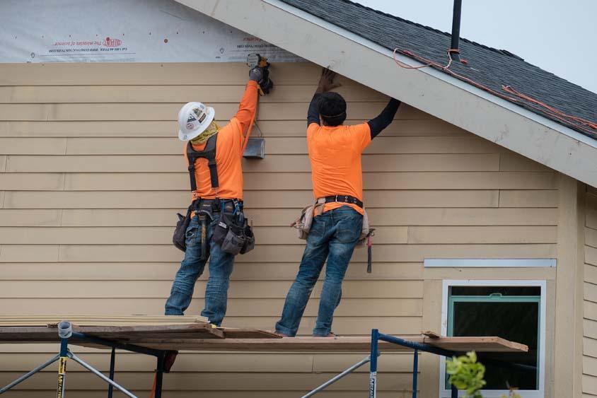 Construction workers installing vinyl siding façade on scaffolding